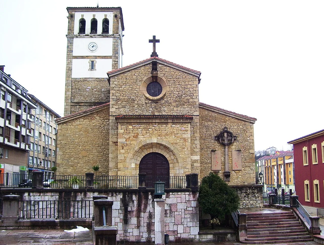 Fachada de piedra de la iglesia de Nava con campanario y cruz en la parte superior.