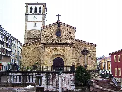 Fachada de piedra de la iglesia de Nava con campanario y cruz en la parte superior.