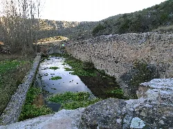 Alberca de Lagüén con agua y vegetación en su interior, junto a un muro de piedra.