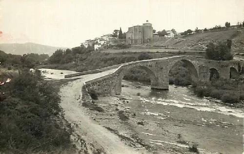 Steinbrücke in Aoiz über einen trockenen Fluss und Häuser auf dem Hügel.