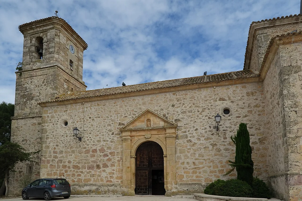 Fachada de una iglesia de piedra con torre y puerta de madera en Villarrubio.