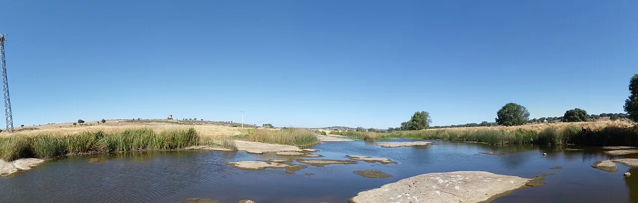 River in El Cubo de Don Sancho with vegetation on its sides and clear sky.