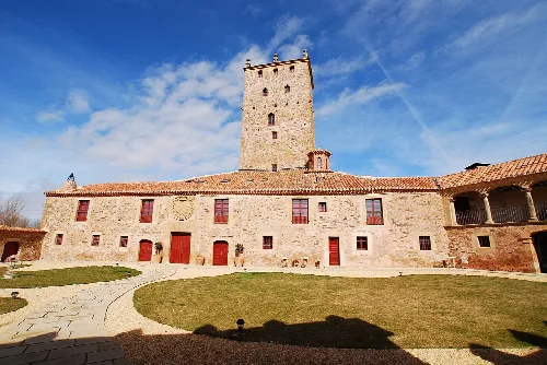 Mittelalterlicher Turm und Gebäude in Aldealseñor mit Himmel und Wolken.
