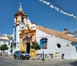 Iglesia blanca con detalles amarillos y torre, decorada con motivos festivos en Castilblanco de los Arroyos.