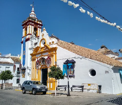 Iglesia blanca con detalles amarillos y torre, decorada con motivos festivos en Castilblanco de los Arroyos.