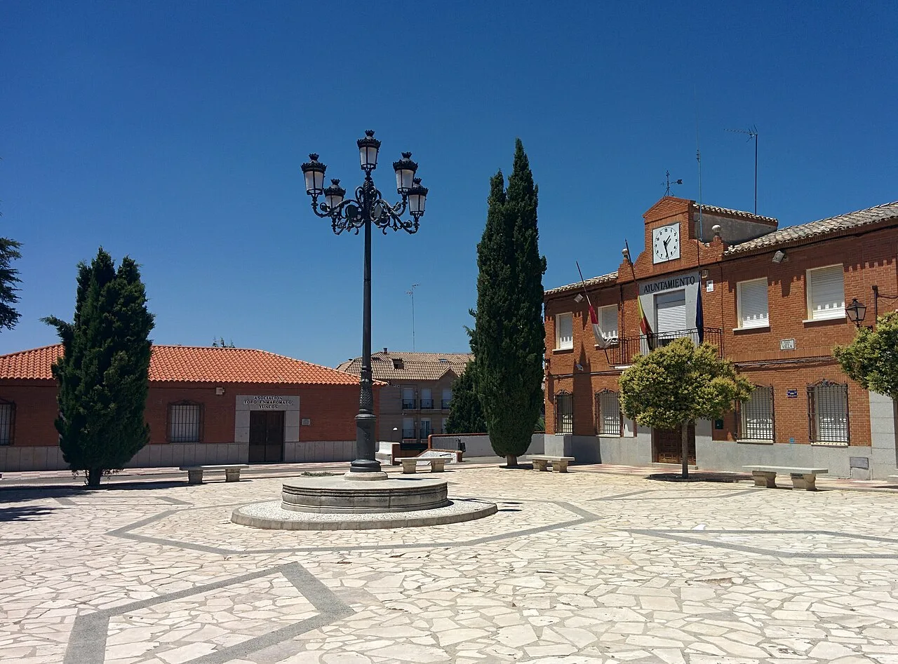 Square with fountain, trees, and a building with a clock in Yuncos.