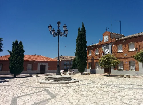 Square with fountain, trees, and a building with a clock in Yuncos.