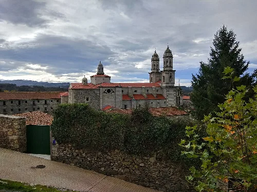 Blick auf das Kloster Sobrado mit Türmen und roten Dächern, umgeben von Vegetation und einer Steinmauer.