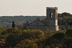 View of the monastery with tower and façade, surrounded by trees and hills.