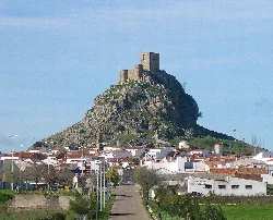 Castle on a hill with white houses and a road in front.