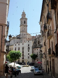 Square with church and bell tower in Bocairente, surrounded by buildings and trees.