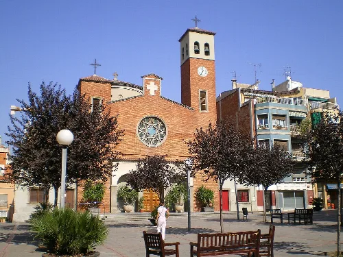 Platz mit Kirche, Bäume, Bänke und eine Frau beim Spaziergang in Sant Adrià de Besòs.