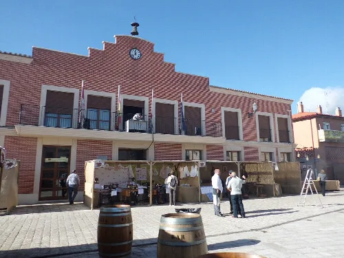 Edificio del ayuntamiento en Villanueva de Duero con personas y barriles en la plaza.