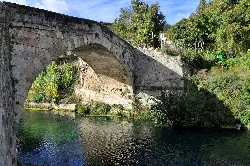 Steinbrücke über den Fluss mit Vegetation und Bäumen.