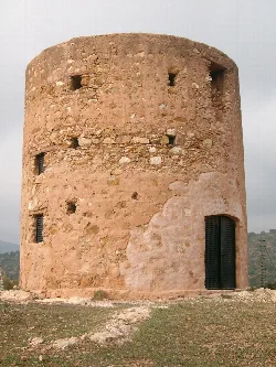 Round stone tower with small windows and black door in a rural setting.