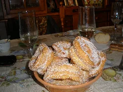 Roscos tradicionales en un plato con azúcar, en una mesa con copas y comida.