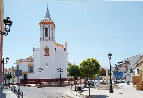 White church with tower and trees in Pilas square.