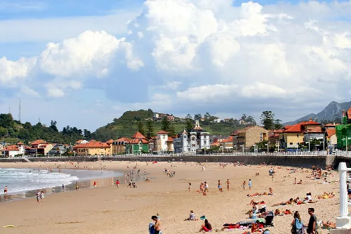Playa con arena, personas y edificios en Ribadesella, Asturias.