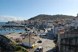 Vista de la villa de Fisterra con puerto y colinas.