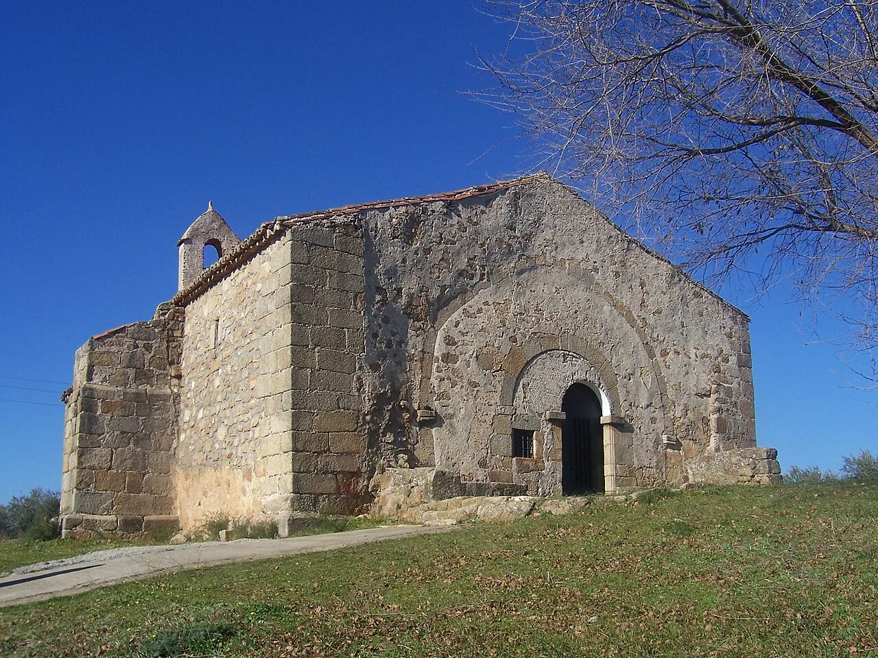 Stone church with arch and black door, in a natural setting with blue sky.