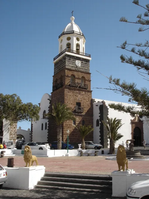 Glockenturm der Kirche San Miguel in Teguise, Lanzarote, mit Palmen und Löwenstatuen.