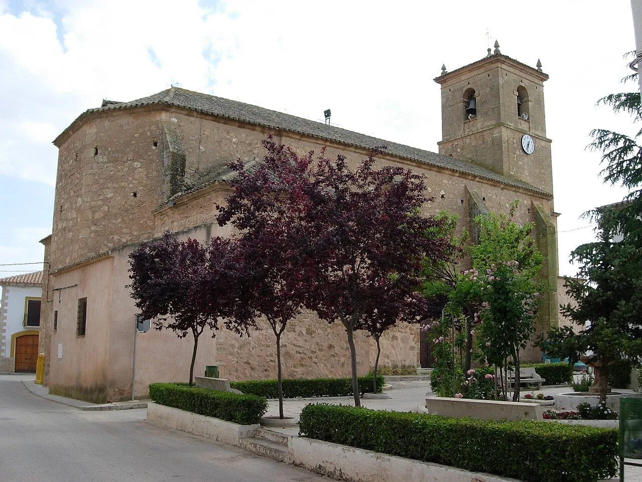 Iglesia de piedra en la plaza del Ayuntamiento con árboles y torre con reloj.