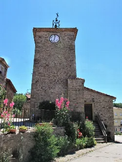 Stone clock tower with flowers and greenery in front.