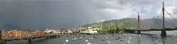 Vista del puerto de Colindres con barcos y un arcoíris en el cielo