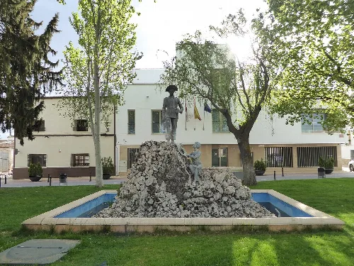 Skulptur in einem Brunnen mit Bäumen und Gebäuden im Hintergrund.