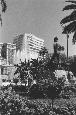 Estatua del Cenachero en la Plaza de la Marina, con palmeras y edificios en el fondo.