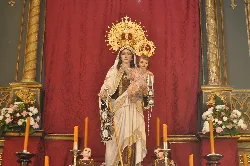 Estatua de la Virgen del Carmen en un altar con velas y flores.