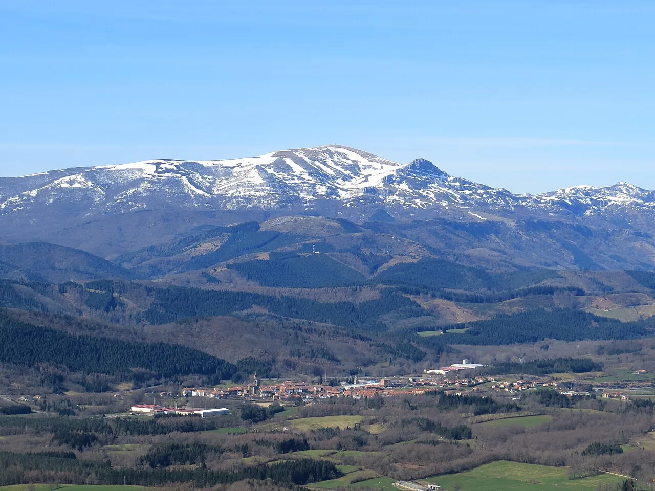 Berg mit Schneebedeckter Spitze und grünes Tal im Vordergrund.