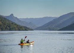 Two people kayaking on a reservoir surrounded by mountains.