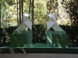 Weiße und grüne geometrische Skulptur in einem Park mit Bäumen.