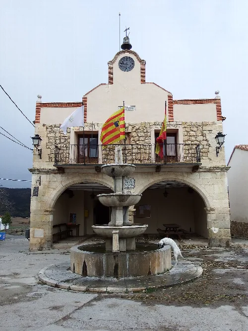 Gebäude mit Uhr, Flaggen und Brunnen auf dem Platz in Moscardón.