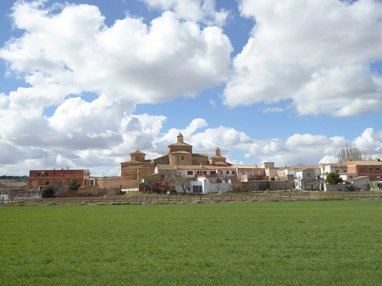 Blick auf eine Stadt mit Kirche und traditionellen Häusern, und ein grünes Feld im Vordergrund.