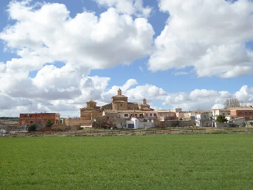 Blick auf eine Stadt mit Kirche und traditionellen Häusern, und ein grünes Feld im Vordergrund.