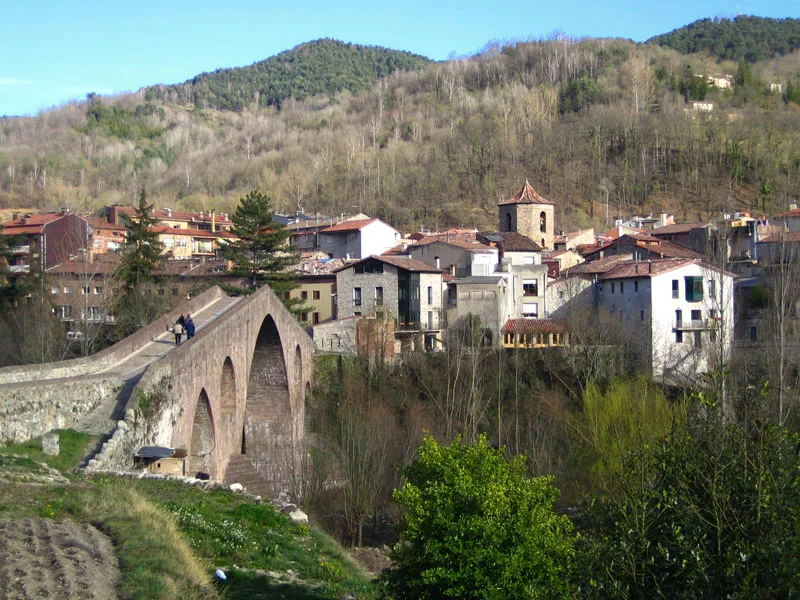 Vista de San Juan de las Abadesas con puente de piedra y casas en las montañas.