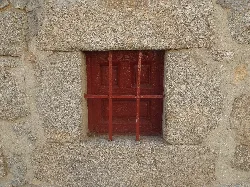 Pequeña ventana con puerta de madera y rejas en una pared de piedra.