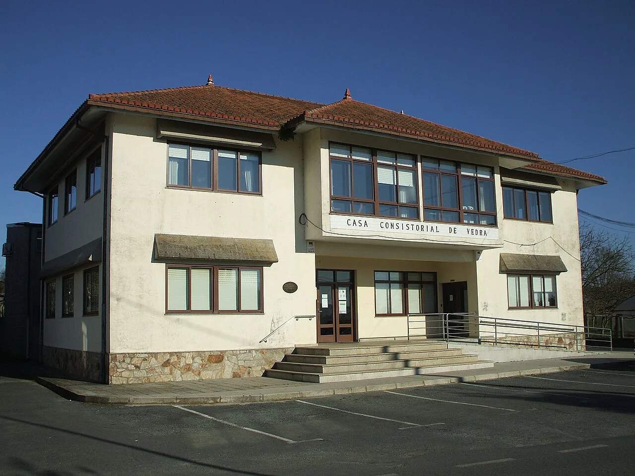 Edificio blanco con ventanas grandes y tejado de tejas rojas.