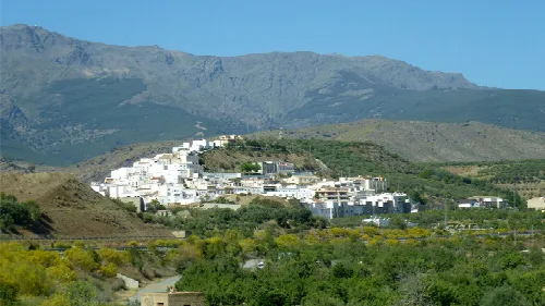 Pueblo blanco en las montañas de Almería con vegetación y picos en el fondo.