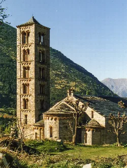 Romanesque church with tower in Valle de Bohí, surrounded by mountains and trees.