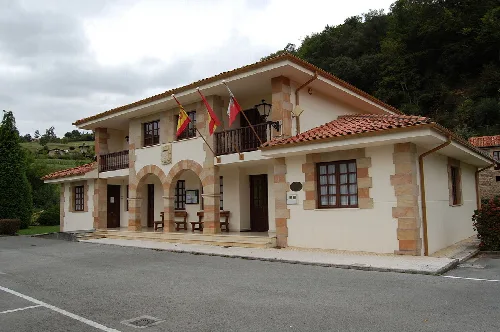 Edificio del ayuntamiento de Herrerías con banderas y entorno rural.