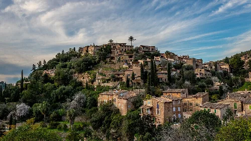 Houses on the hillside of Deyá with greenery and blue sky.