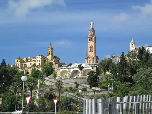 Edificio con torre alta y otras construcciones en una colina con vegetación.