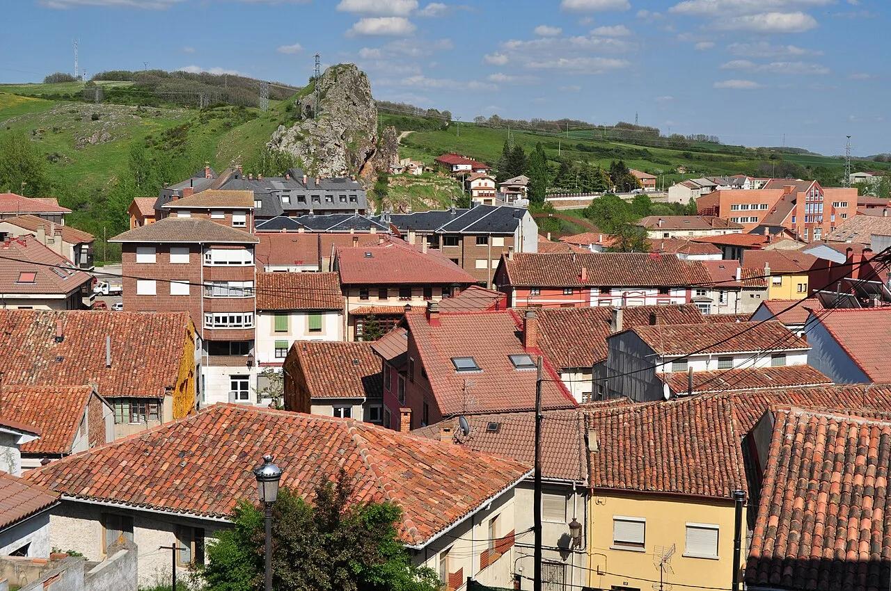 Houses with tiled roofs in Cervera de Pisuerga, with green hills and rocks in the background.