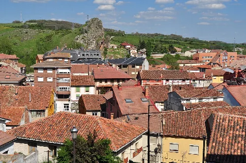 Houses with tiled roofs in Cervera de Pisuerga, with green hills and rocks in the background.