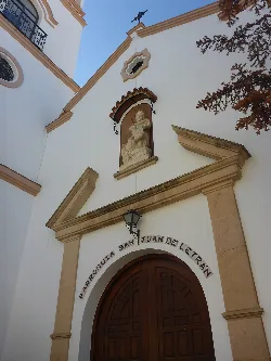 Church facade with sculpture and wooden arch in Arriate.
