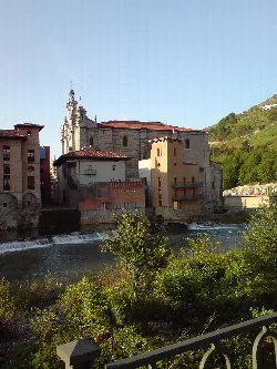 Molino y iglesia de Santa María en Tolosa, con río y vegetación.