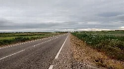 Straight road in a flat landscape with cloudy sky.